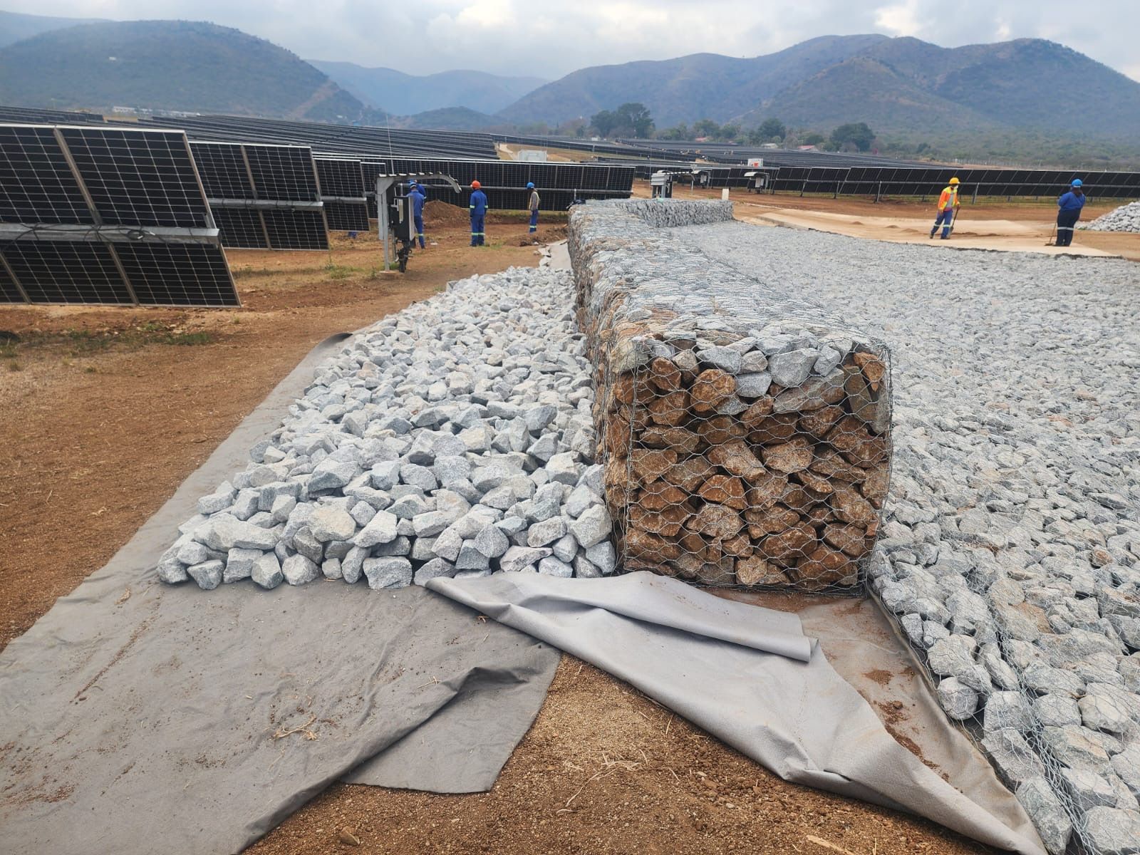 Rock-filled gabion and stone apron on geotextile between rows of solar panels at Balfour